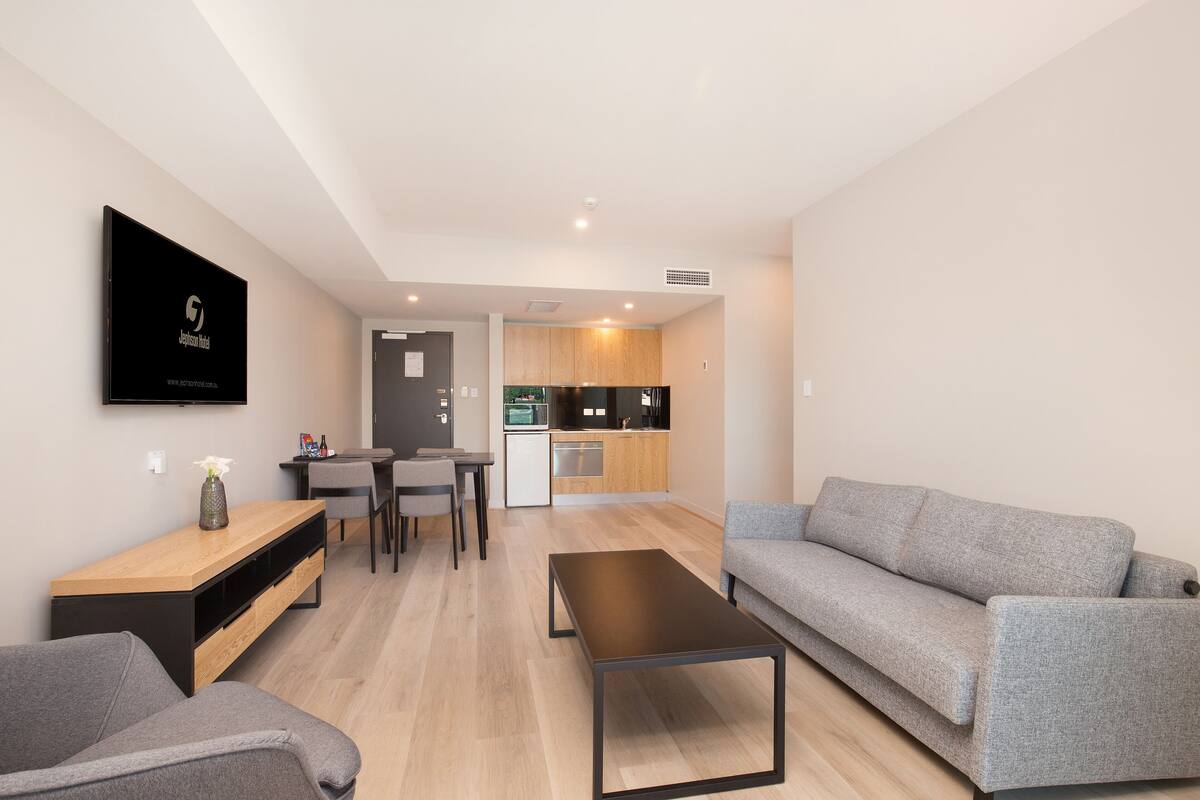 A modern living room with a grey sofa, a wooden coffee table, and a TV mounted on the wall.