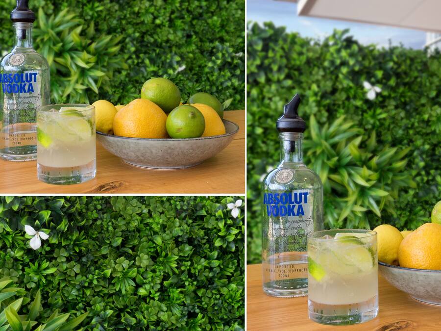 A bottle of Absolut Vodka, a glass of vodka with lime, and a bowl of lemons and limes.