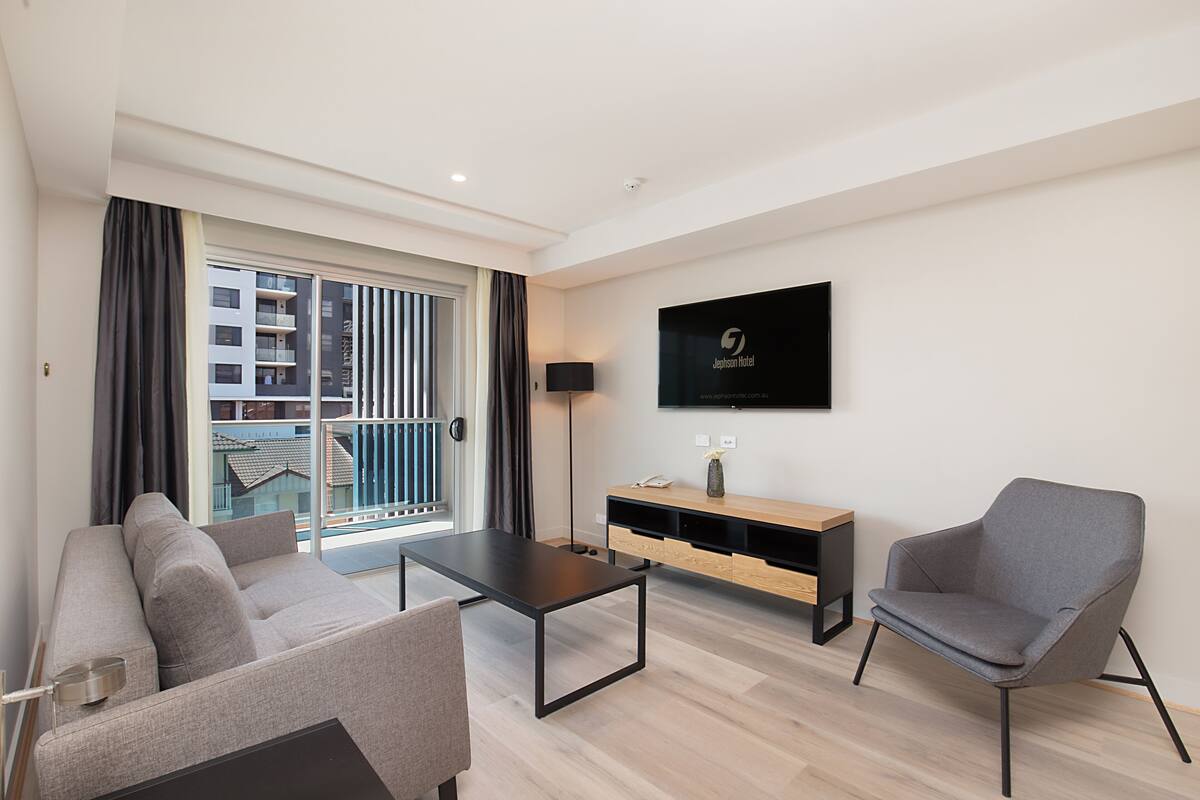A modern living room with a sofa, a coffee table, a TV mounted on the wall, and a view of the outside balcony.