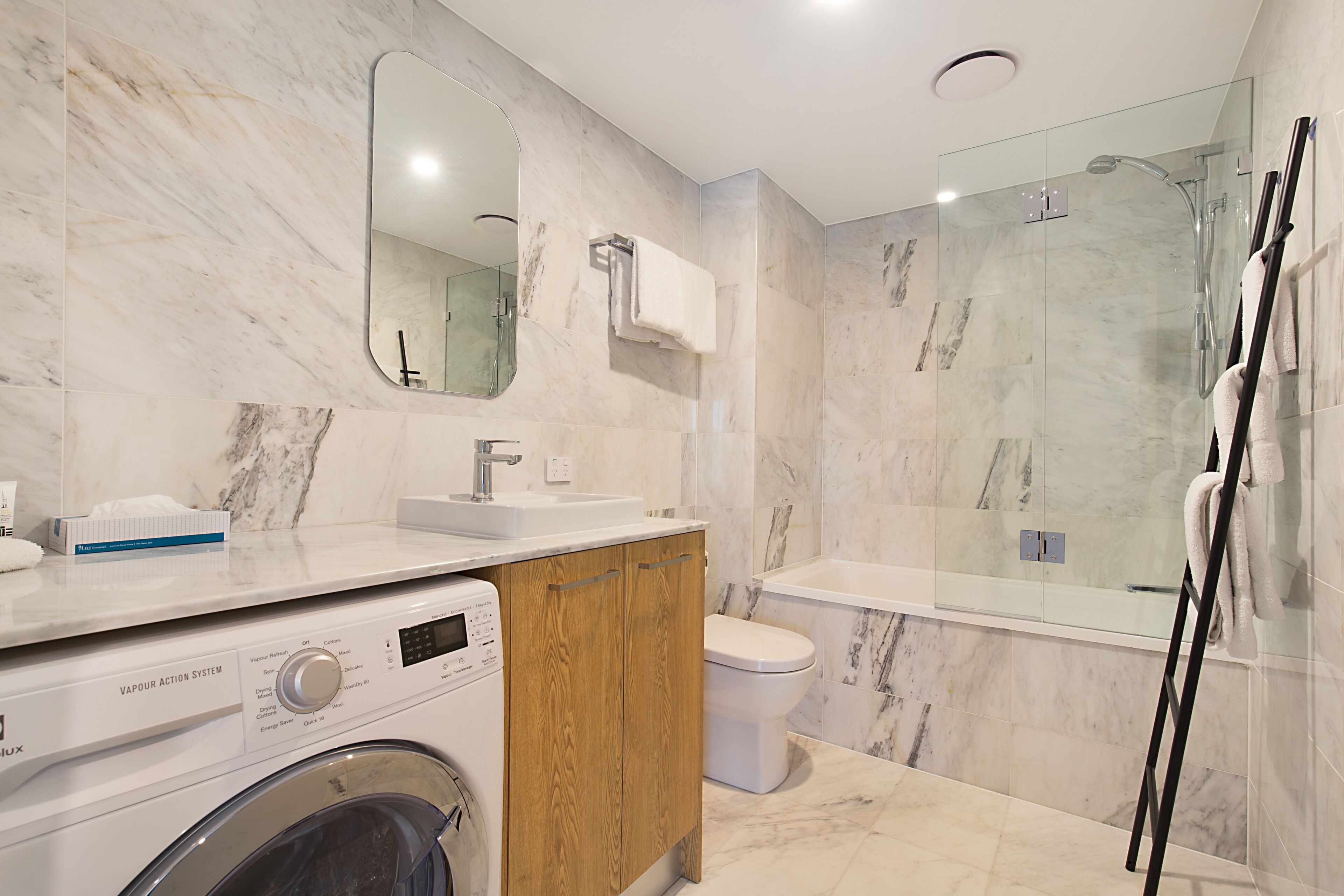 A modern bathroom with a marble floor, a built-in washing machine, a toilet, and a glass-enclosed shower area.