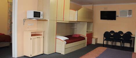 Habitación de hotel compacta con literas, microondas, televisión y un pequeño escritorio.