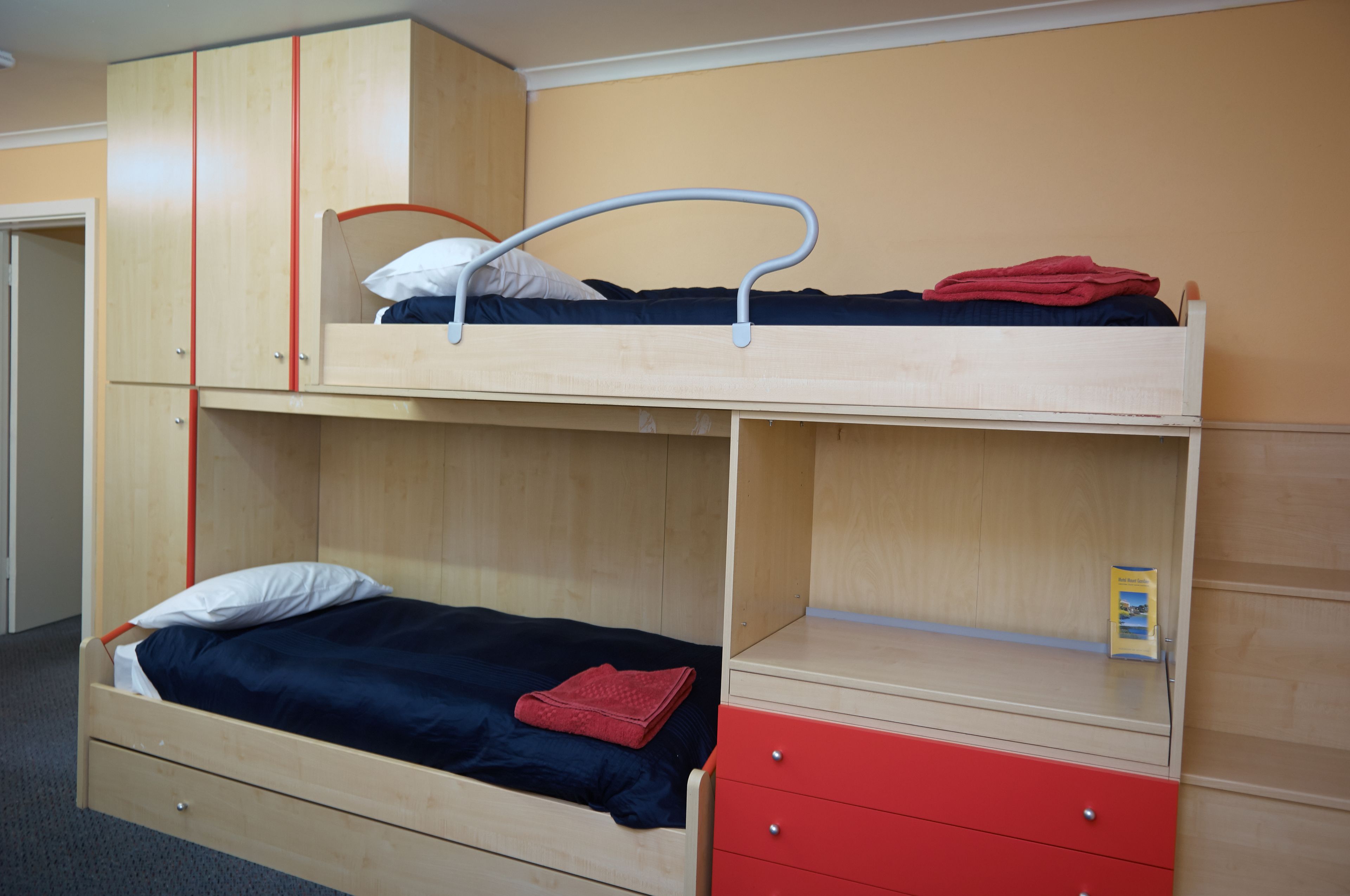 Una cama litera con un módulo de cajones rojo y una cama individual abajo.