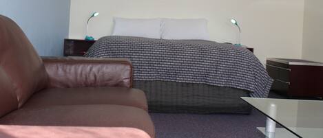 A bedroom with a bed, a brown leather chair, a bedside table with a lamp, and a dresser.