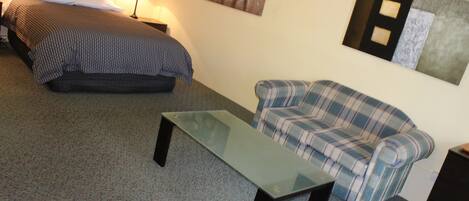 A room with a bed, a sofa, a glass-top table, and a wall-mounted artwork.