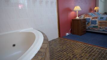 Une salle de bain avec une baignoire, un espace de douche carrelé et un lit avec une couette.