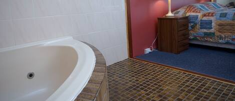 A bathroom with a bathtub, a tiled shower area, and a bed with a quilt.