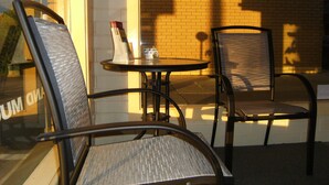 A cafe with two metal chairs and a small round table, a brick wall, and a window with a reflection. - Motel Mount Gambier (Mount Gambier)