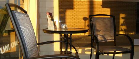 A cafe with two metal chairs and a small round table, a brick wall, and a window with a reflection.