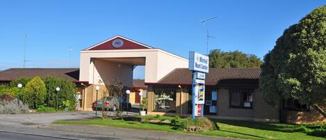Un motel con techo rojo y paredes color crema, un letrero y un estacionamiento.