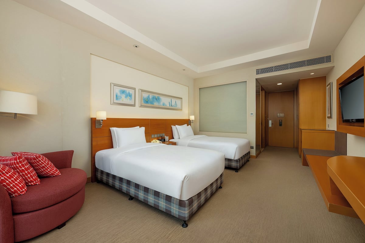 A hotel room with two beds, a red sofa, a TV, and artwork on the wall.
