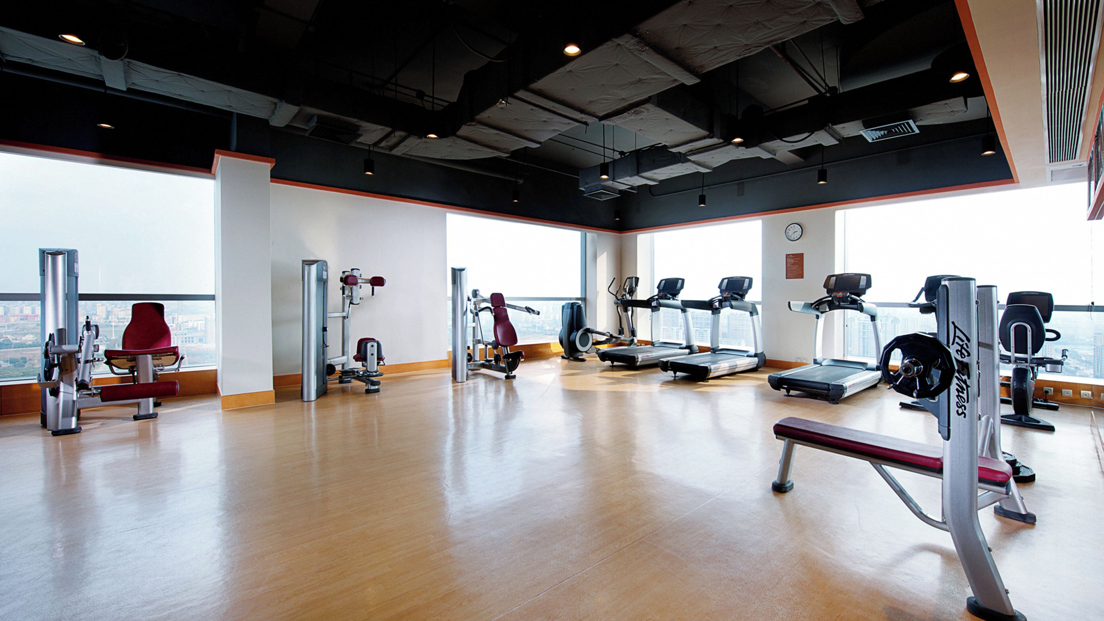 A gym with various exercise equipment, large windows, and a view of the city.