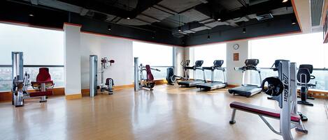 A gym with various exercise equipment, large windows, and a view of the city.