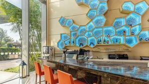 Uma área de bar moderna com uma luminária hexagonal, uma máquina de café e banquetas de bar laranja.