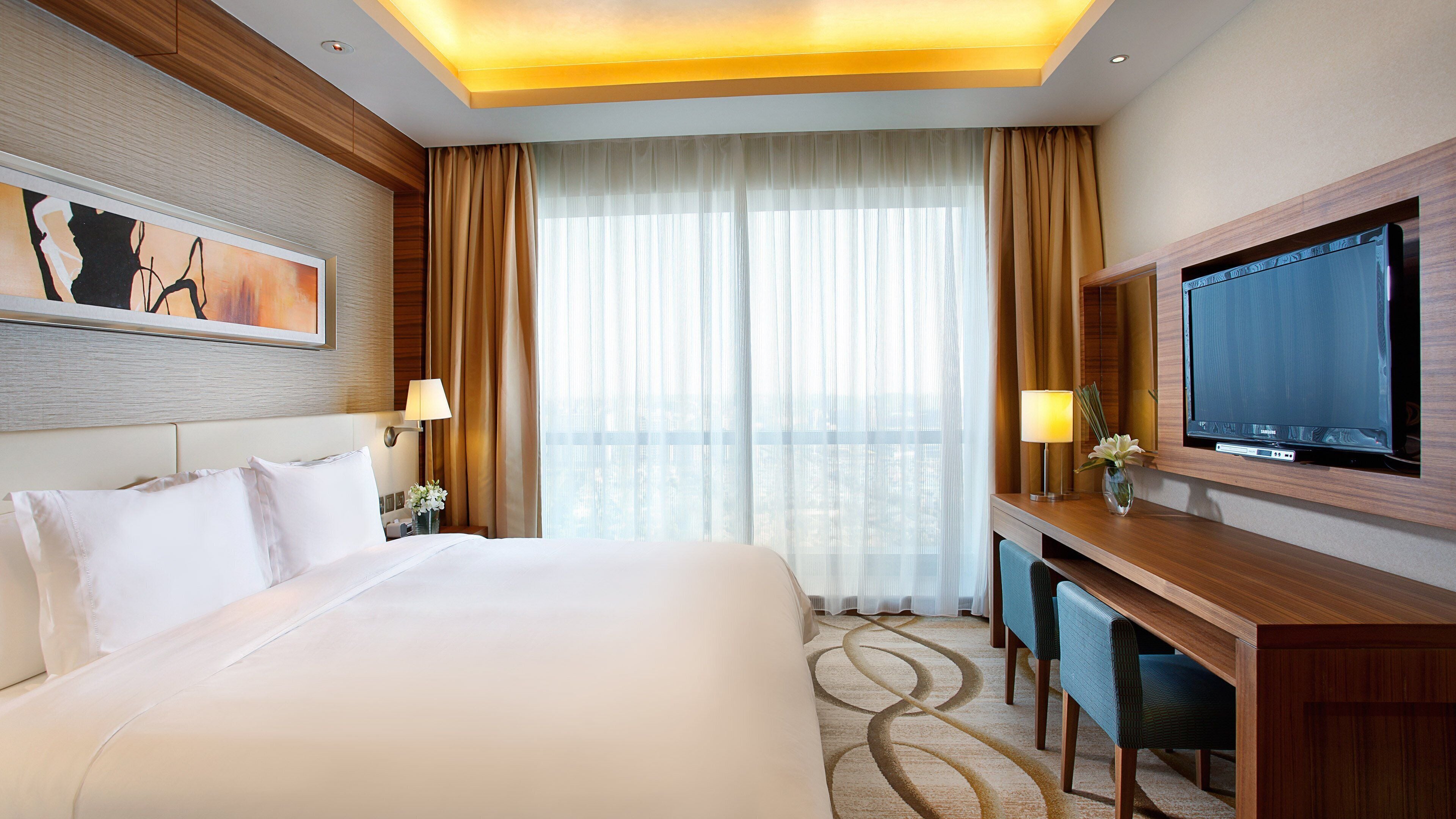 Habitación de hotel con una cama grande, un escritorio con televisor y vistas a la ciudad desde la ventana.