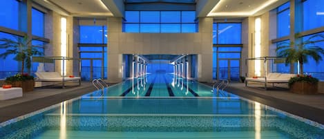 An indoor swimming pool with clear lanes, large windows, and a high ceiling.