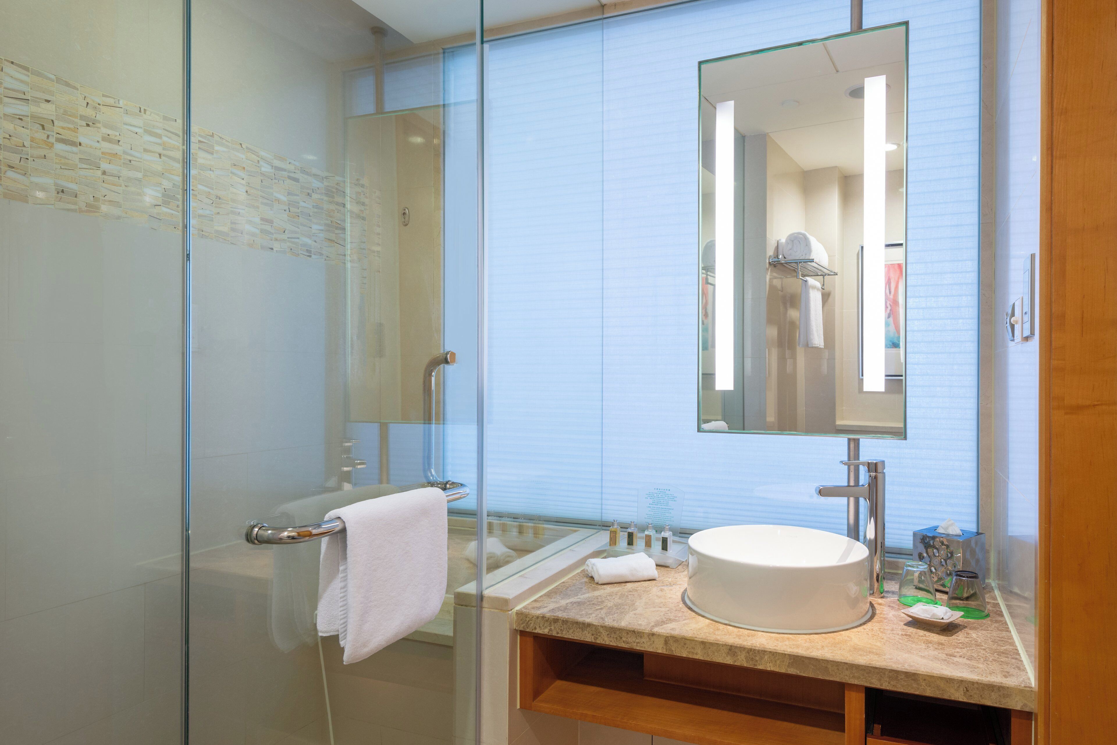 Un baño moderno con cabina de ducha de vidrio, un lavabo blanco y un espejo sobre el mostrador.