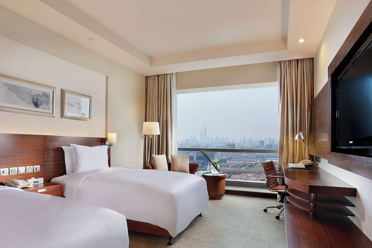 A hotel room with two beds, a desk, a chair, a TV, and a city view.