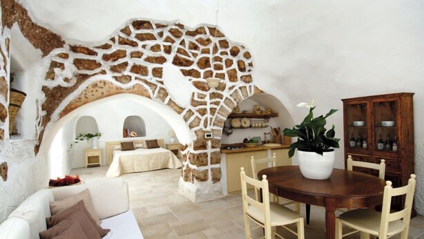 Una sala acogedora con un arco de piedra, una mesa de comedor con sillas, un sofá y un mueble con botellas.