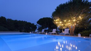 Una piscina con sillones de descanso y un árbol adornado con luces.