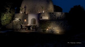 Un edificio de piedra con una estructura circular, una pequeña mesa con sillas y plantas en macetas.