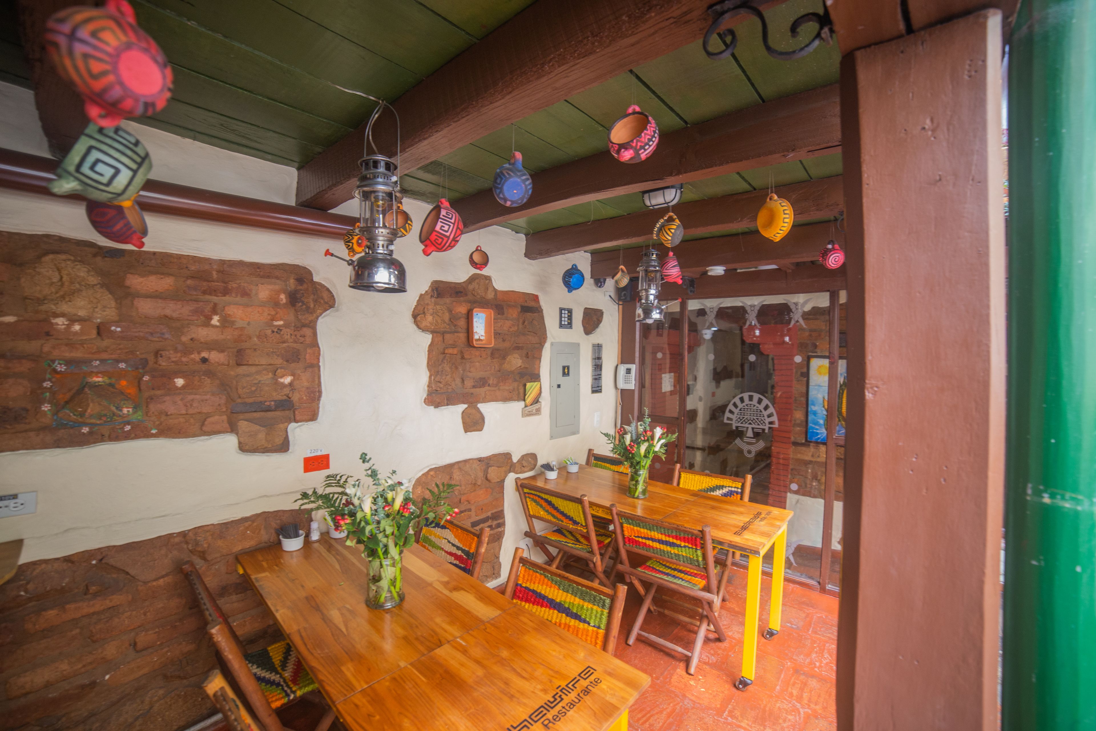 A rustic dining area with wooden tables and chairs, a brick wall, and hanging decorative items.