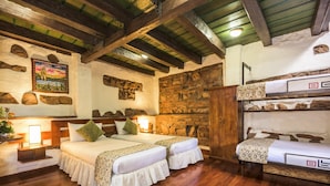 A cozy room with two beds, a stone wall, wooden beams, and a bunk bed. - Hotel Muisca (Bogotá)