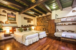 Una habitación acogedora con dos camas, una pared de piedra, vigas de madera y una cama individual sobre otra.
