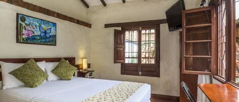 Un dormitorio con cama, escritorio, silla, televisor y ventana con contraventanas.
