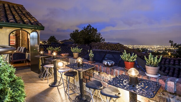 An outdoor patio with a stone table and chairs, potted plants, and a view of the city at dusk. - Hotel Muisca (Bogotá)