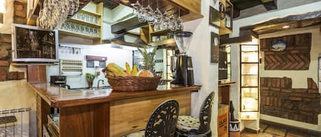 A rustic bar area with wooden furniture, a fruit basket, and hanging wine glasses.