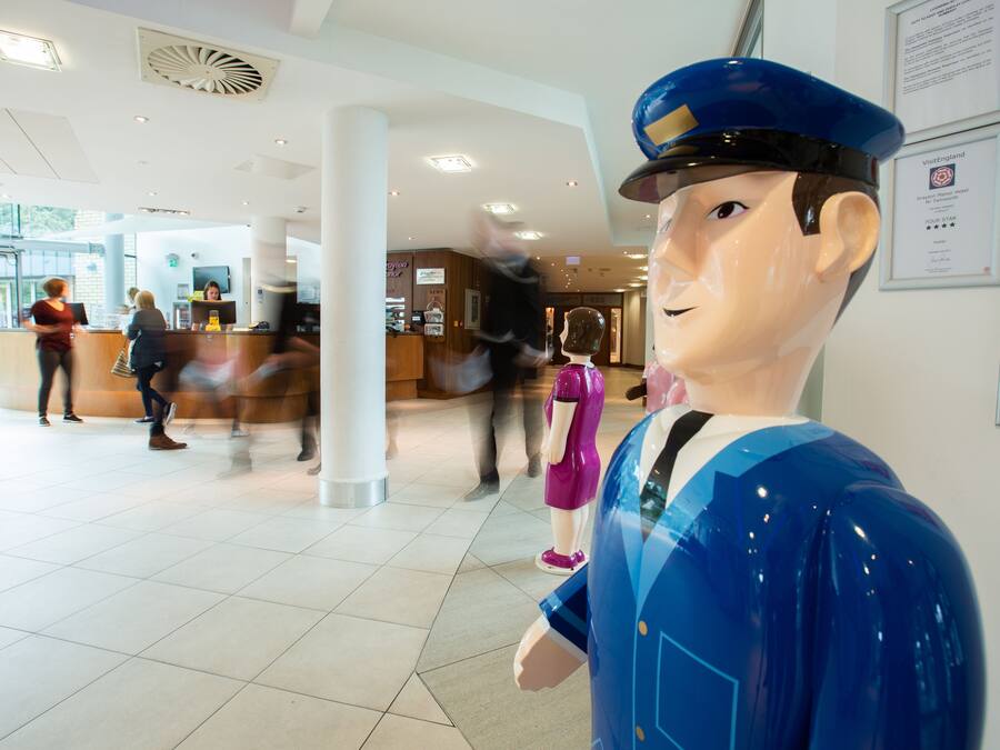 Zona de recepción con una gran estatua azul, un mostrador y algunas personas.