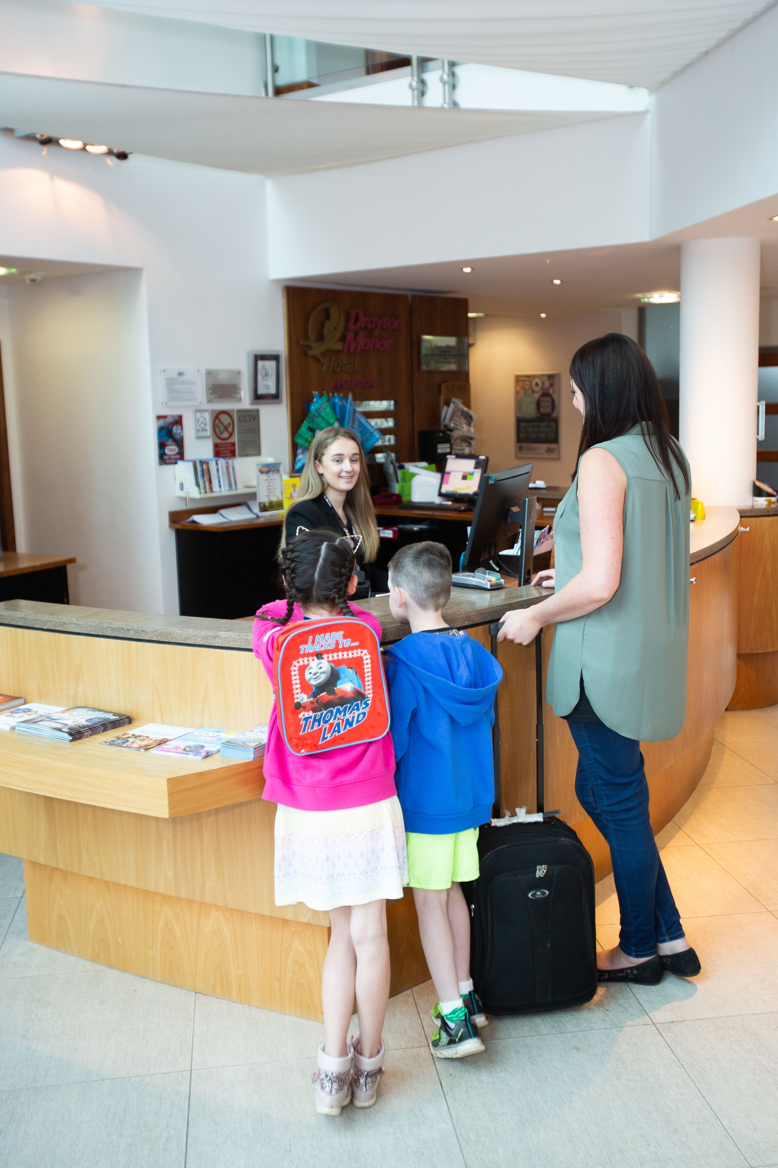A reception desk in a hotel lobby with a counter, a computer, and a seating area in the background.