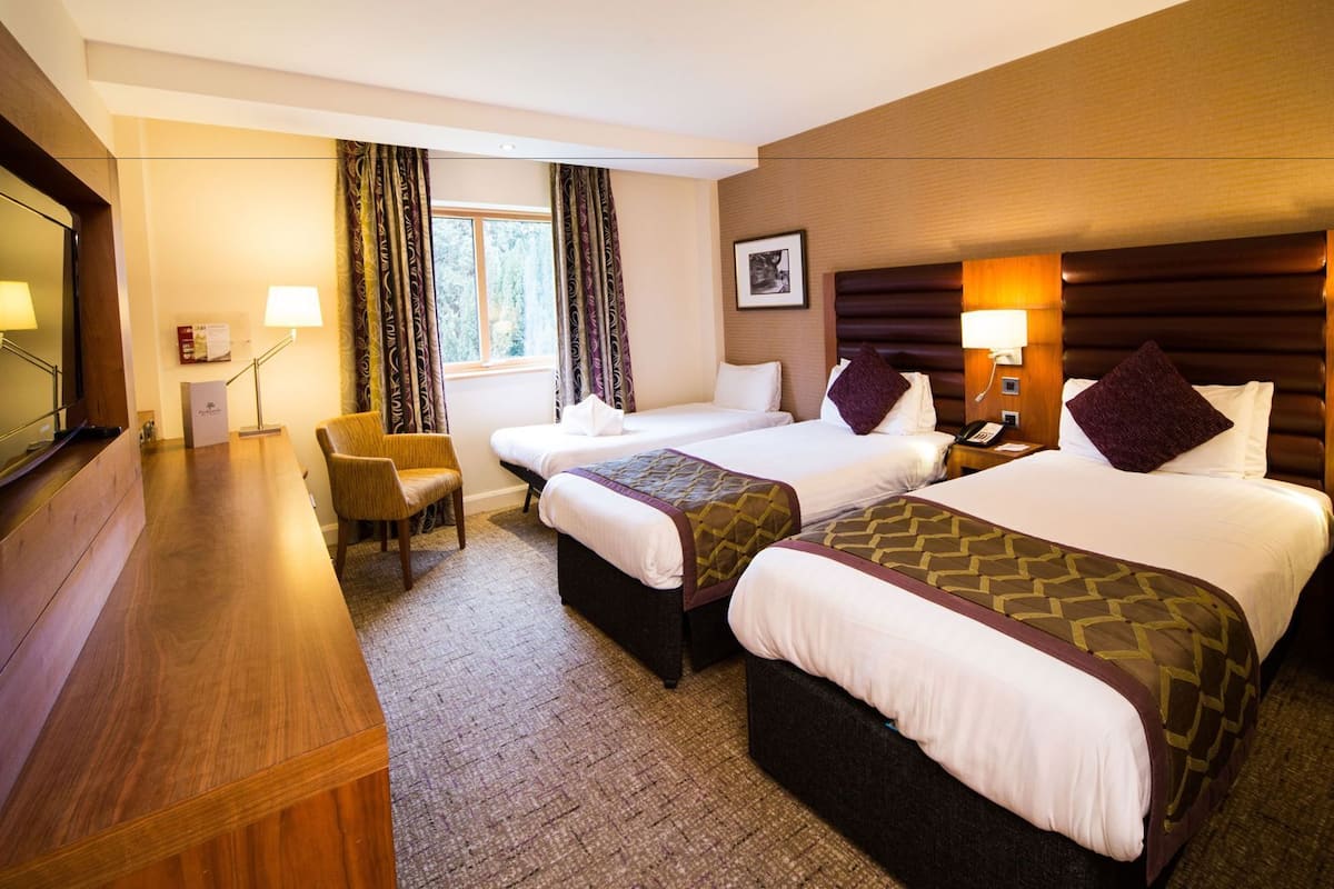 A hotel room with two beds, a desk, a chair, a TV, and a window with curtains.