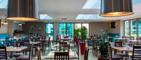 A spacious restaurant with high ceilings, skylights, and a variety of seating arrangements including tables and chairs.