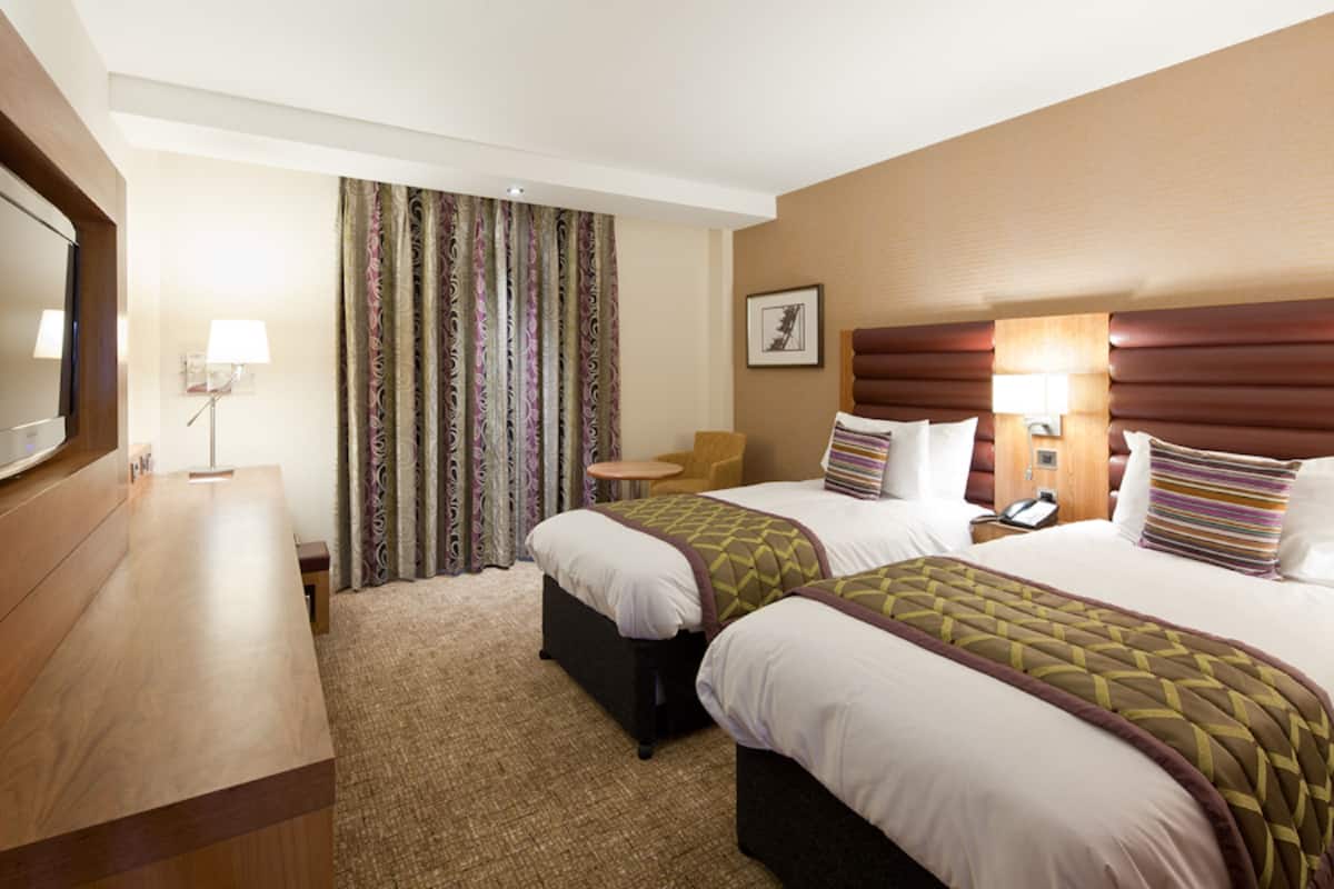 A hotel room with two beds, a desk, a chair, a TV, and a window with curtains.