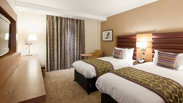 A hotel room with two beds, a desk, a chair, a TV, and a window with curtains.