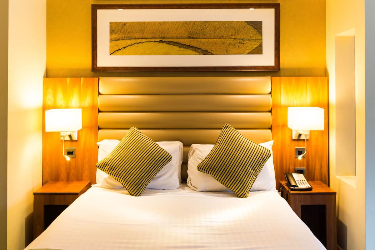 A hotel room with a large bed, two bedside lamps, a telephone, and a framed picture on the wall.