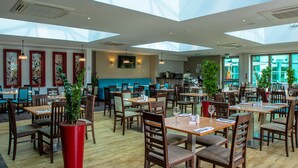 A spacious restaurant with high ceilings and skylights, wooden tables and chairs, and potted plants. - Drayton Manor Hotel (Tamworth)