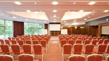 Un salón de conferencias con filas de sillas anaranjadas, una pantalla grande y una chimenea.