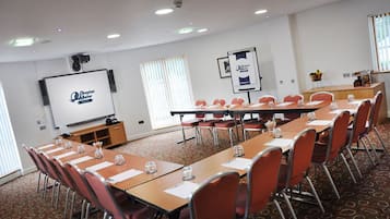 Una sala de conferencias con una larga mesa, sillas, una pantalla de proyector y una pizarra.