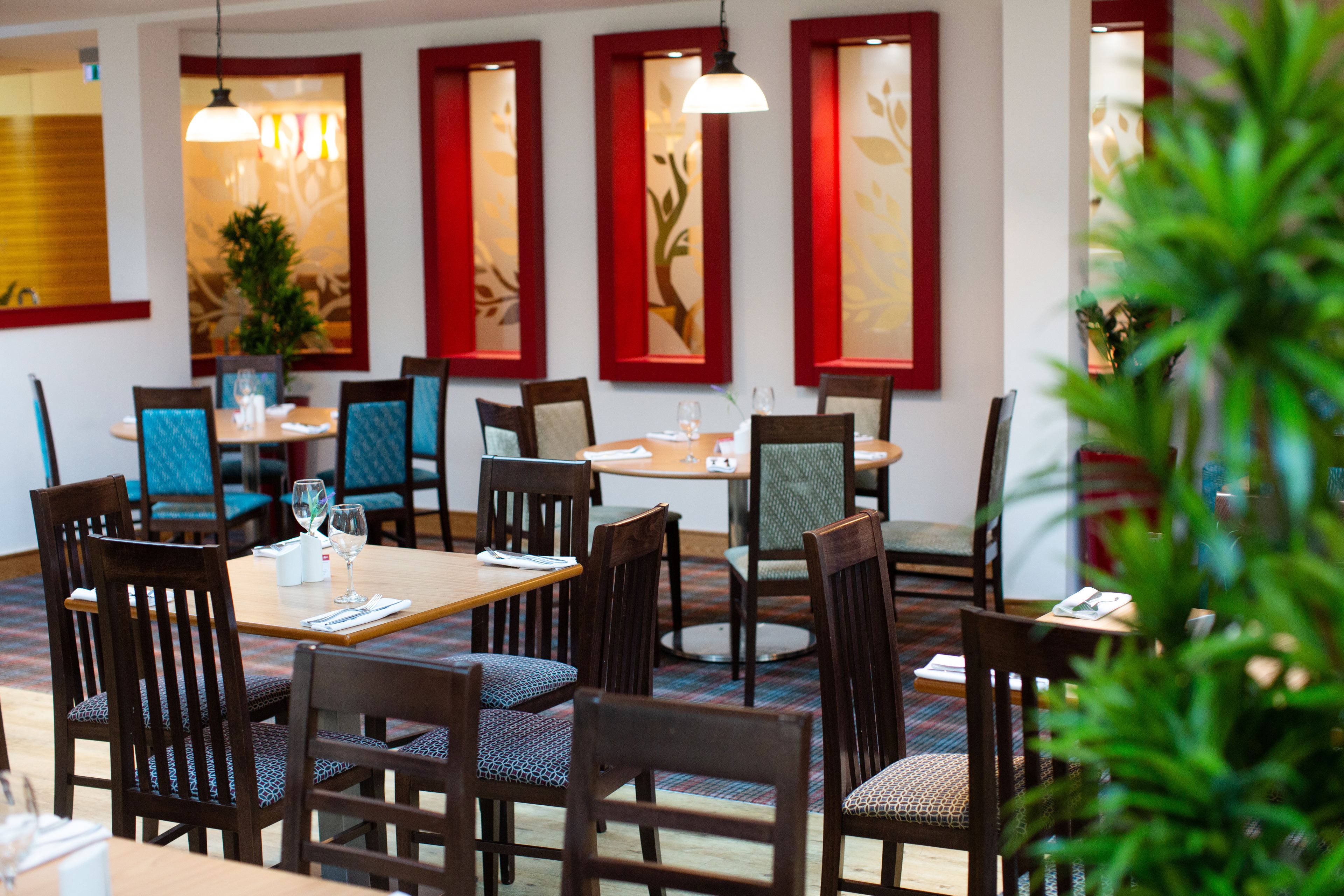 Un restaurante con mesas y sillas de madera, ventanas con marcos rojos y lámparas colgantes.
