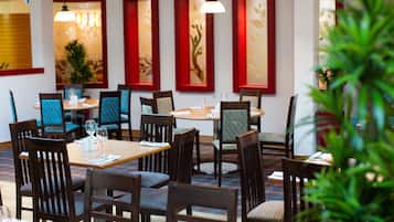 Un restaurante con mesas y sillas de madera, ventanas con marcos rojos y lámparas colgantes.