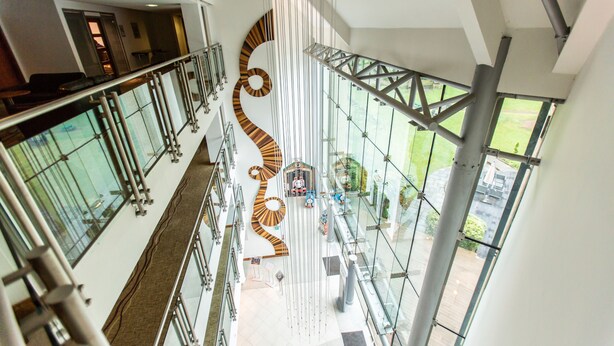 A modern interior with a glass atrium, a distinctive spiral design on the ceiling, and a view of the outdoors through large windows. - Drayton Manor Hotel (Tamworth)