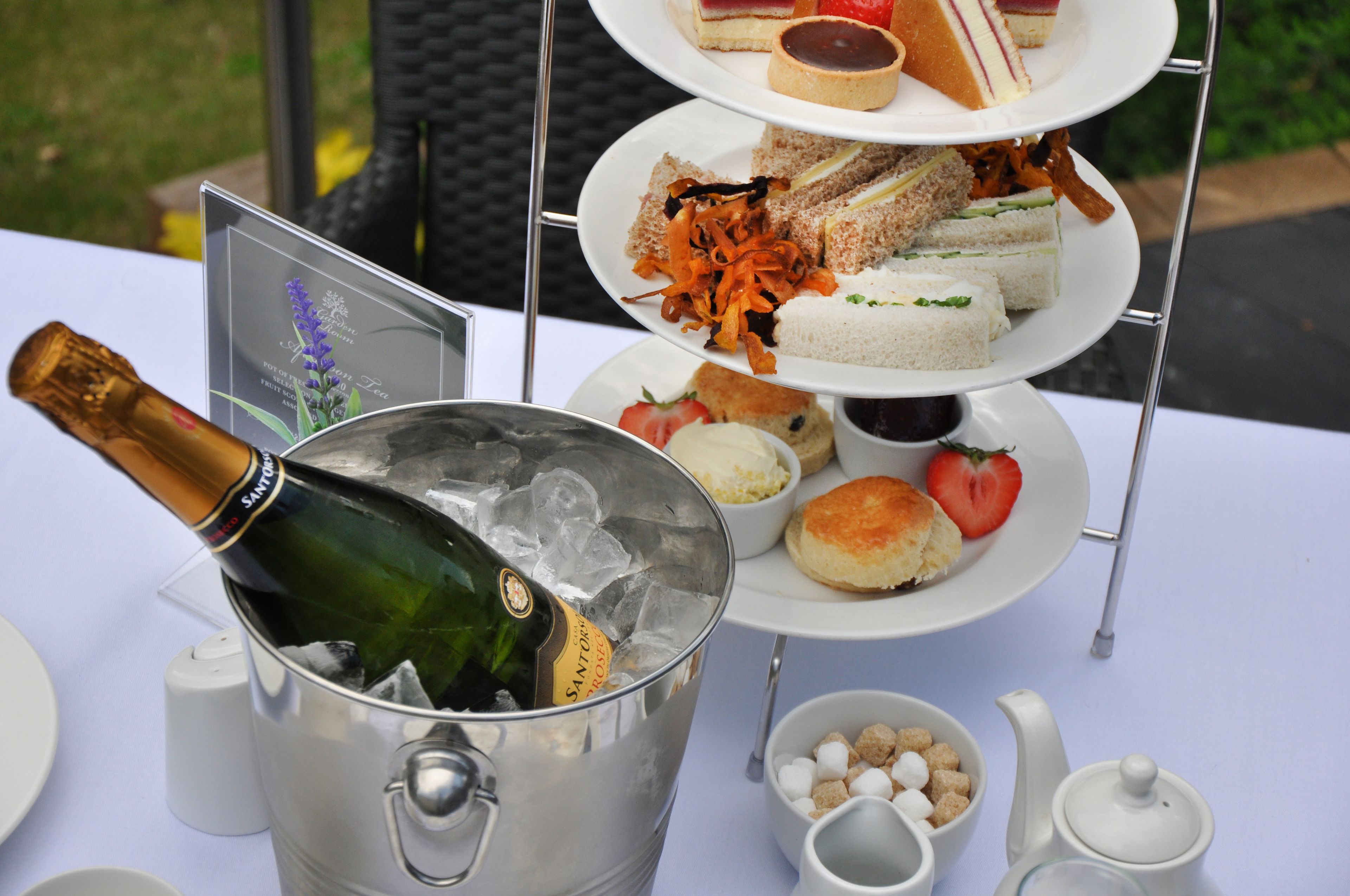 A three-tiered dessert stand with various sandwiches and a bottle of champagne in an ice bucket.