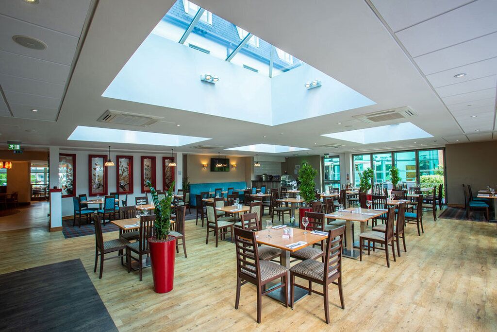 Un restaurant spacieux avec de hauts plafonds et des puits de lumière, un plancher en bois, ainsi que plusieurs tables et chaises.