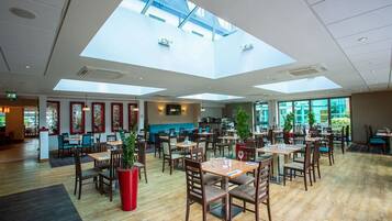 A spacious restaurant with high ceilings and skylights, wooden flooring, and several tables and chairs.