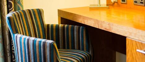 A striped armchair, a wooden desk, a lamp, and a wall-mounted picture in a hotel room.