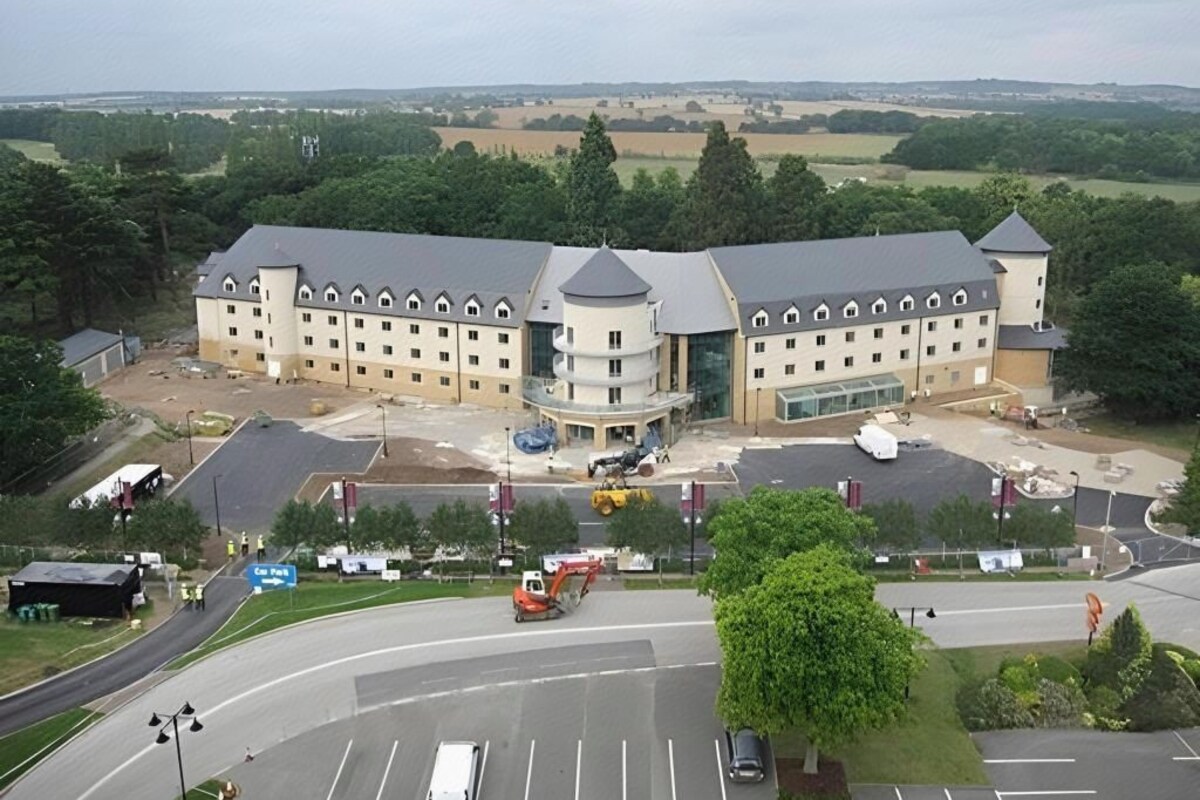 A large building with multiple wings and a central tower, surrounded by a parking lot and a road.
