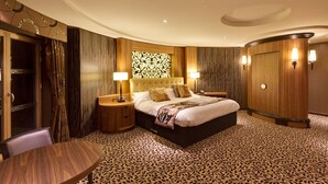 A luxurious bedroom with a large bed, two bedside tables with lamps, a round wooden table, and a patterned carpet. - Drayton Manor Hotel (Tamworth)