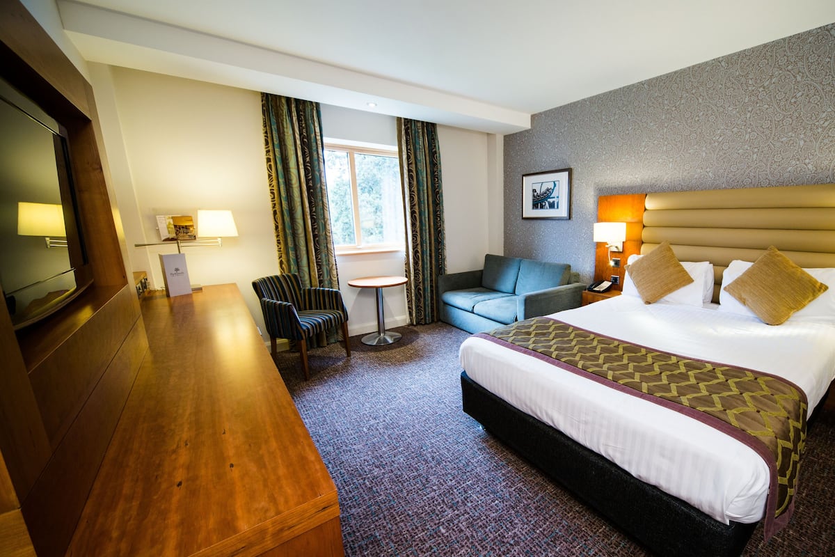 A hotel room with a large bed, a desk, a chair, a sofa, and a small table.